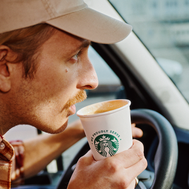 Man med kaffekopp i en bil.